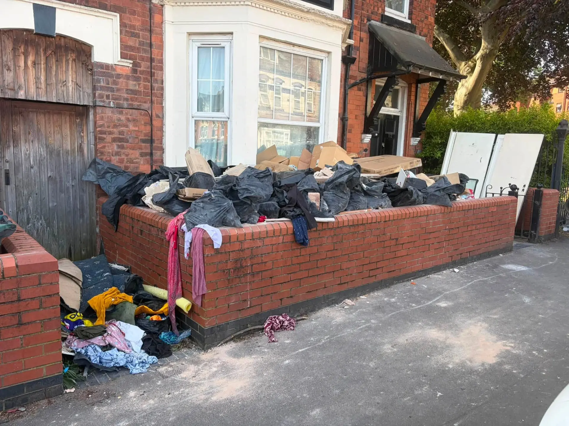 Bags of household waste, boxes and clutter piled against the front garden wall